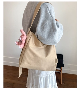 Detail view of large beige canvas tote bag with a pink plush rabbit charm on broad strap
