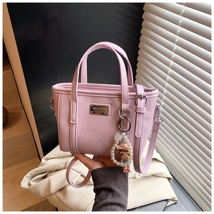Detail der rosa Handtasche mit Litschi-Struktur, Logo-Plakette und Perlenanhänger