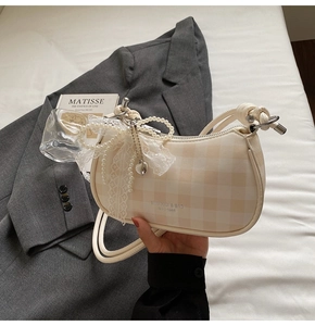 Détail du sac à carreaux avec chaîne en perles et élégant nœud en dentelle blanche