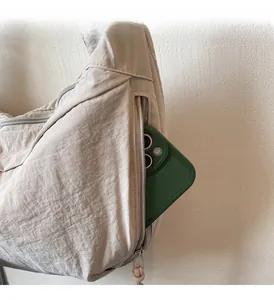Detail view of a side zipper pocket on a beige dumpling bag holding a green mobile phone