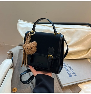 Detail of black matte flap backpack with golden buckle and brown bear charm