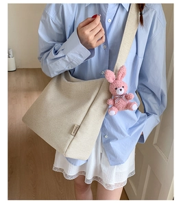 Detail of beige canvas tote bag with a pink plush rabbit charm and fashion label