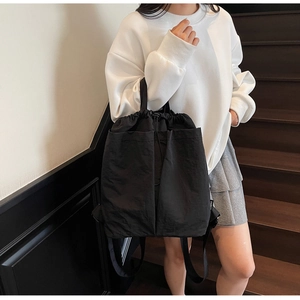 Detail of black nylon drawstring backpack with two front pockets on a model