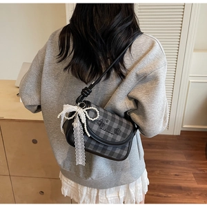 Detail of checkered shoulder bag with lace bow and pearl chain on a female model