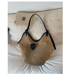 Detail of hobo straw tote bag featuring black leather trim and long shoulder strap