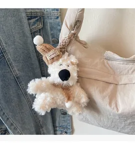 Close-up of a cute white plush bear charm with a brown knit hat and scarf on a bag