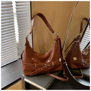Detail of caramel brown crescent bag with glossy finish and metal buckle decoration