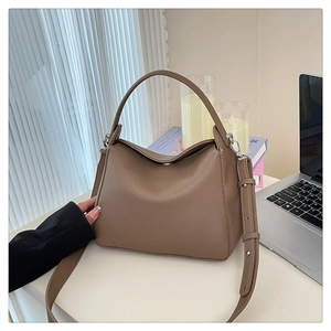Detail of taupe lychee grain leather handbag with silver hardware on a desk