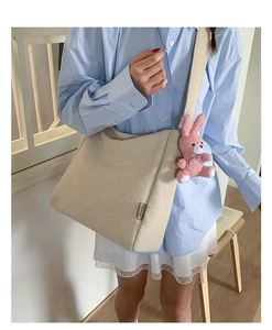 Detail of beige canvas tote bag with fashion label and pink plush rabbit charm accessory