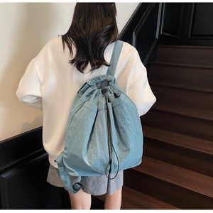 Detail of light blue drawstring backpack with adjustable straps on a minimalist background