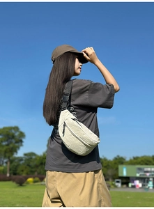 Detail of off-white nylon waist bag with adjustable strap worn by model outdoors