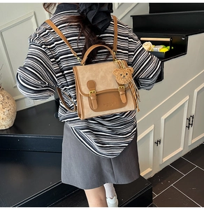 Back view of a vintage beige backpack with brown leather trim on a female model