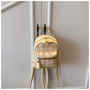 Gros plan d'un mini sac à dos à carreaux jaune et blanc suspendu à une poignée blanche