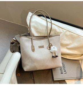 Detail of beige tote bag with plush charm and brand tag on white leather surface
