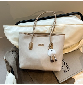 Detail of grey suede tote bag with brown leather handles and plush monster charm