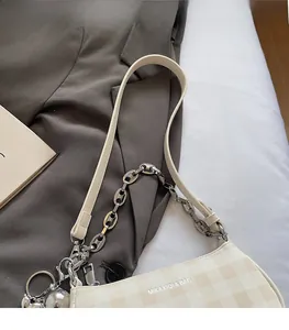 Detail of beige checkered crossbody bag with silver chain strap on a grey blazer