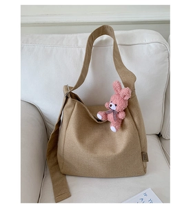 Detail of khaki canvas hobo bag with pink plush keychain on white sofa fabric