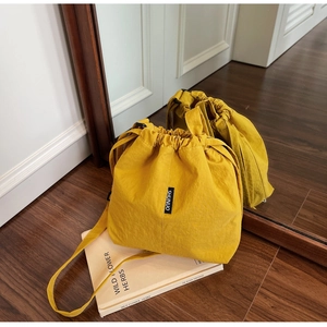 Detail of a bright yellow drawstring bucket bag with SHUNUO label on wooden floor