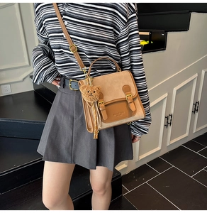 Detail of college style brown crossbody bag with plush bear charm and buckle straps