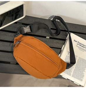 Detail of a bright orange nylon waist bag with a large black buckle and brand label