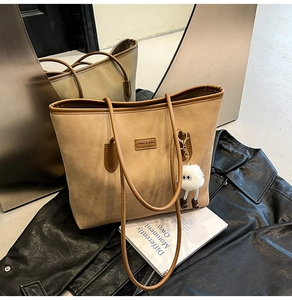 Close-up of beige suede tote bag with brown leather trim and fluffy monster charm