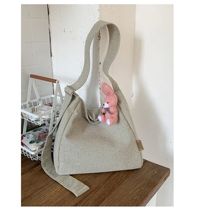 Detail of light green canvas tote bag featuring wide strap and pink rabbit charm