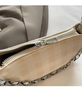 Macro detail of silver metal zipper and chain on beige checkered crossbody bag