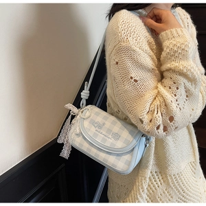 Detail of blue plaid crossbody bag featuring lace bow and pearl charm on a model