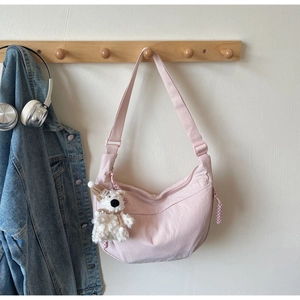 Pink crescent crossbody bag hanging on a hook with a cute teddy bear charm detail