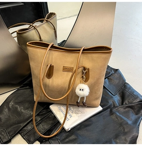 Detail of khaki and brown tote bag with plush charm on a lifestyle background