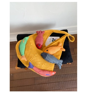 Detail of yellow knit crochet tote bag featuring colorful fish plush charms inside