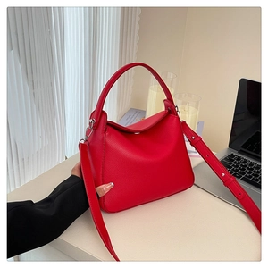 Detail of red lychee grain leather handbag with adjustable strap on a minimal desk