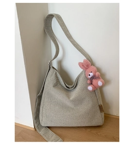 Detail of oat-colored canvas hobo bag with wide strap and pink plush rabbit charm