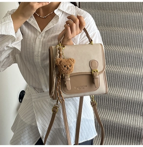 Detail of khaki beige leather handbag featuring a gold buckle and brown plush bear charm