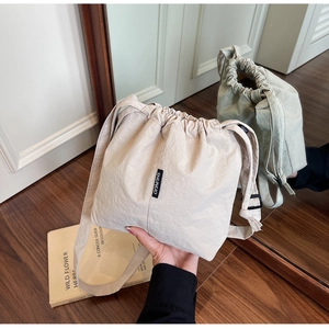 Detail of beige nylon drawstring bucket bag with adjustable strap and brand label