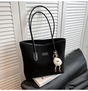 Detail of black suede tote bag with plush monster charm on minimalist leather surface