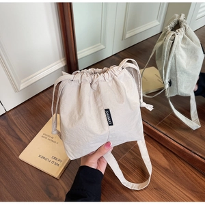 Detail view of beige drawstring bucket bag with black woven logo on lightweight fabric