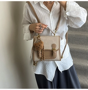 Close-up of retro color-block handbag with brown plush bear charm and magnetic buckles