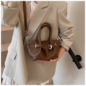 Détail du sac seau en cuir marron foncé avec bandoulière réglable et boucle décorative