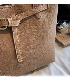 Close-up of tan lychee grain leather with white contrast stitching and gold metal ring buckle