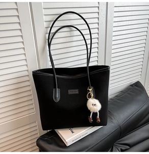 Close-up of black tote bag with leather straps and a cute white monster plush charm