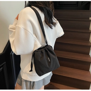 Detail of black drawstring bucket bag with textured fabric and logo on a wooden staircase