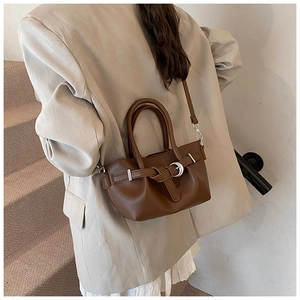 Détail d'un sac à main marron mat avec boucle argentée et anses rondes porté par un mannequin