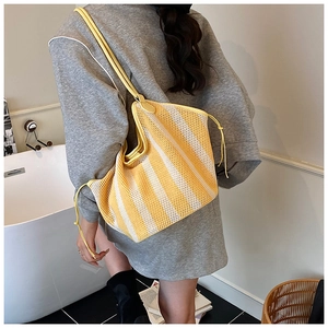 Detail of yellow and white striped mesh tote bag worn by a model in casual setting
