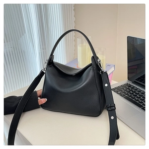 Close-up of black lychee-textured leather handbag with wide shoulder strap on a desk