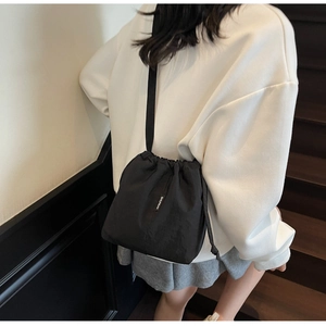 Close-up of black drawstring bucket bag in nylon showing logo patch and sleek strap