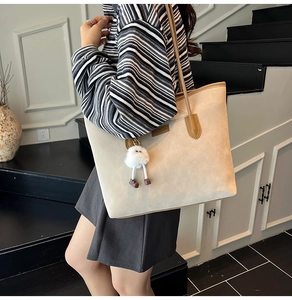 Detail of beige suede tote bag with brown leather straps and white plush pendant