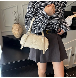 Detail of beige suede shoulder bag with dual adjustable straps and embossed logo on model