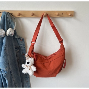 Detailed view of orange nylon crescent bag with adjustable strap and cute bear charm