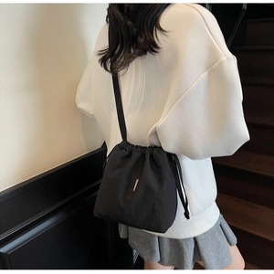 Close-up of minimalist black drawstring bucket bag with adjustable nylon shoulder strap